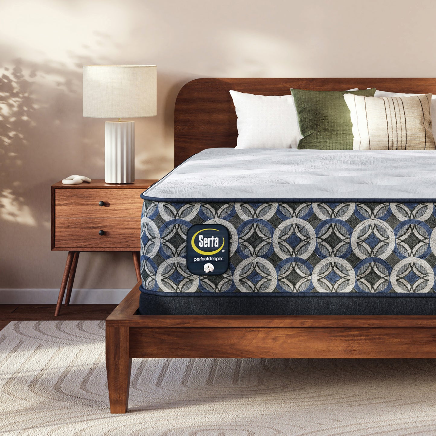 Serta perfect sleeper plush mattress on a wooden bed frame in a bedroom setting with a lamp and nightstand.