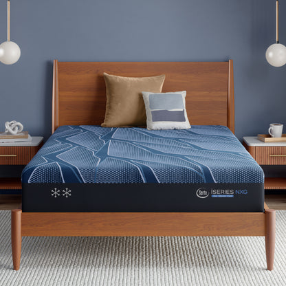 Blue Serta iSeries NXG mattress on a wooden bed frame with pillows against a blue wall.
