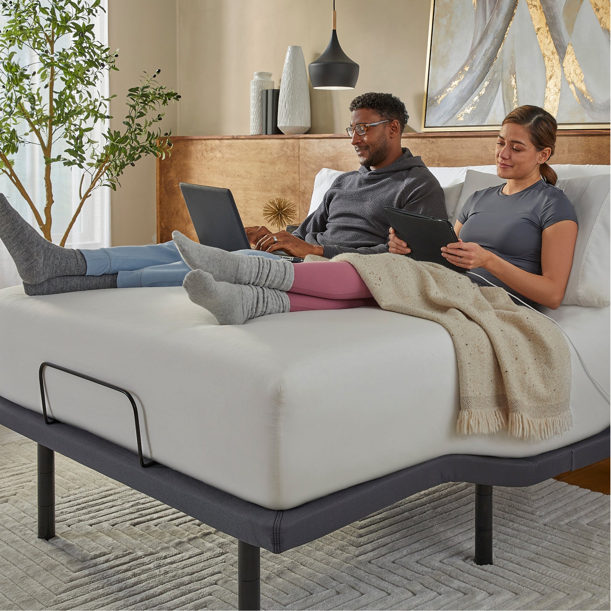 Man and Woman sitting in a Baselogic Gold Adjustable Base with a white mattress on top of it.