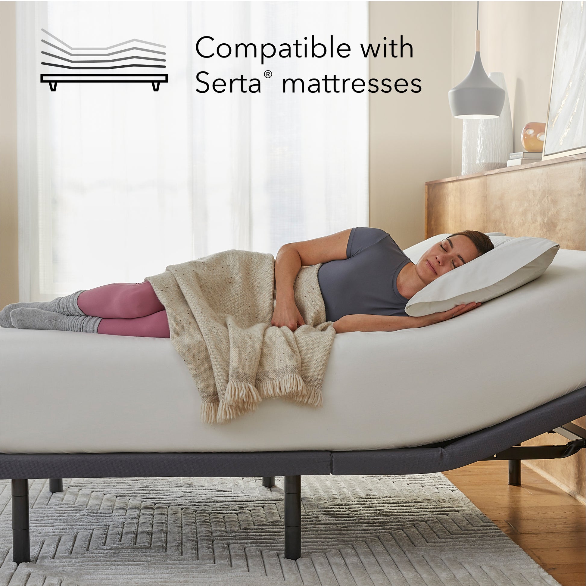 Woman lying on a Beautyrest mattress on top of a Pearl adjustable base with a pillow, surrounded by a blanket, in a bedroom setting.